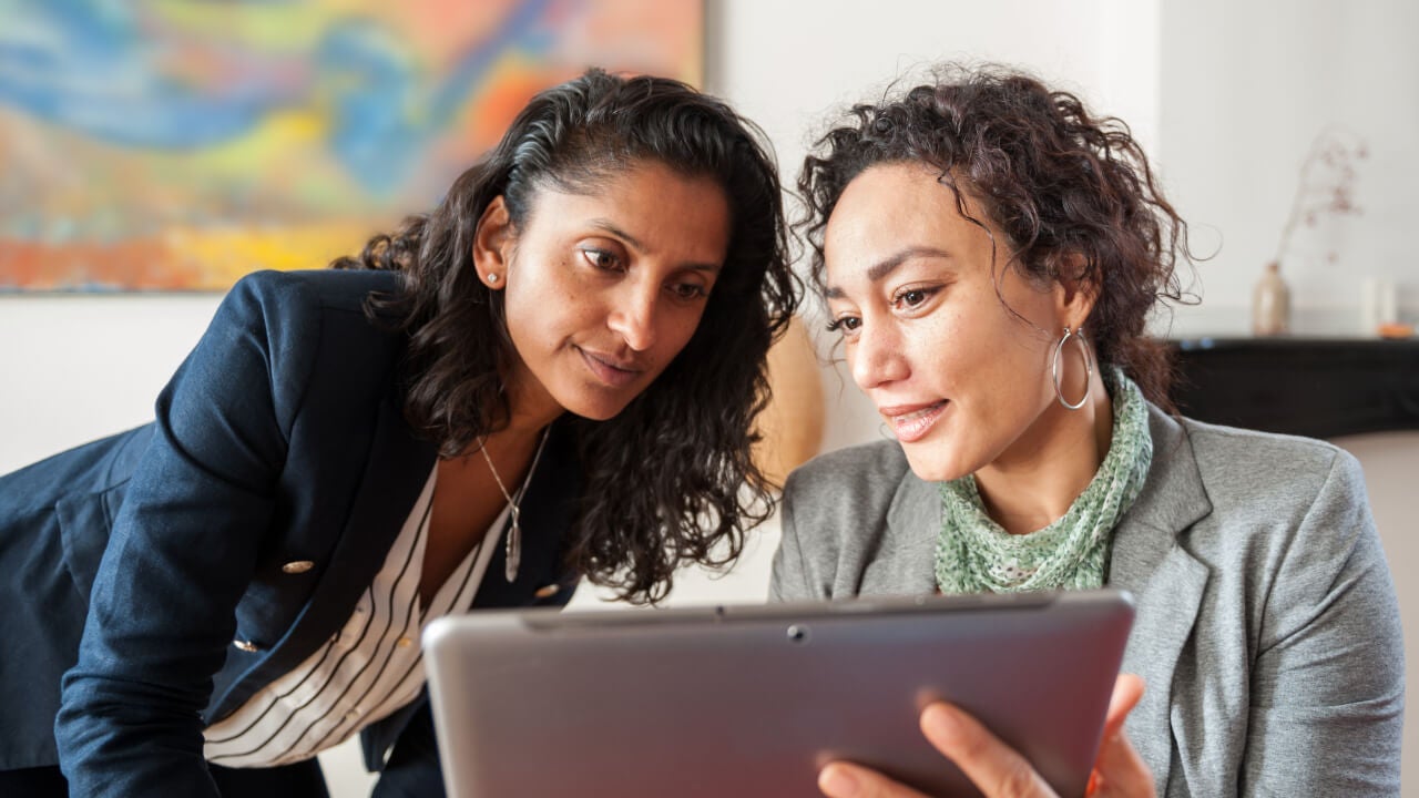 Two business women look at an ipad together.