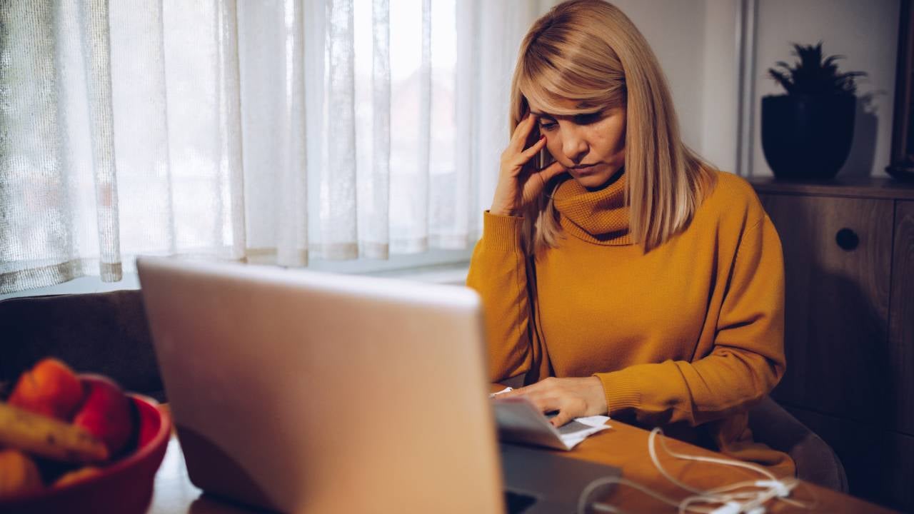 Stressed mature woman reading news on laptop at home.