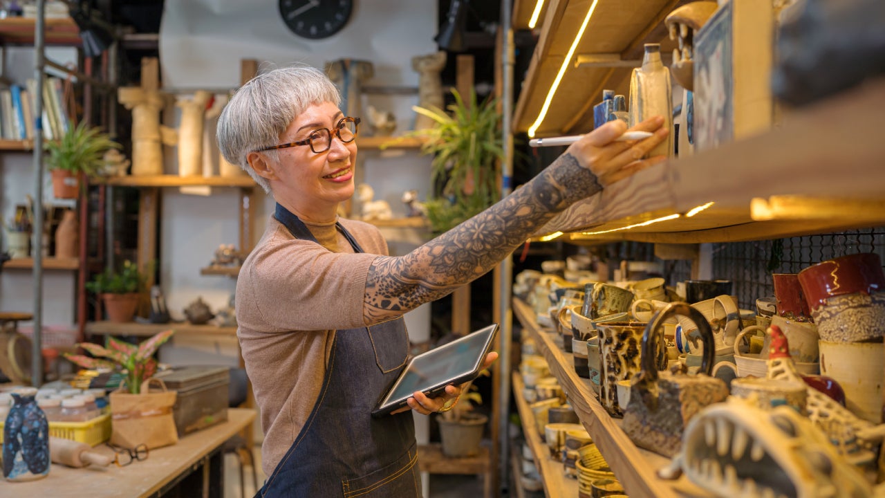 artist woman using digital tablet for stock counting on pottery shop