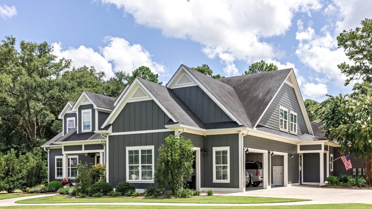 A large gray craftsman new construction house with a landscaped yard and leading pathway sidewalk