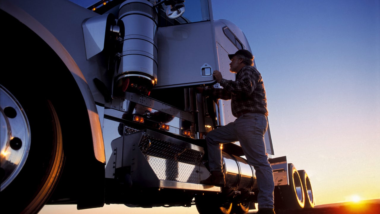 A truck driver getting into his semi truck at dawn.