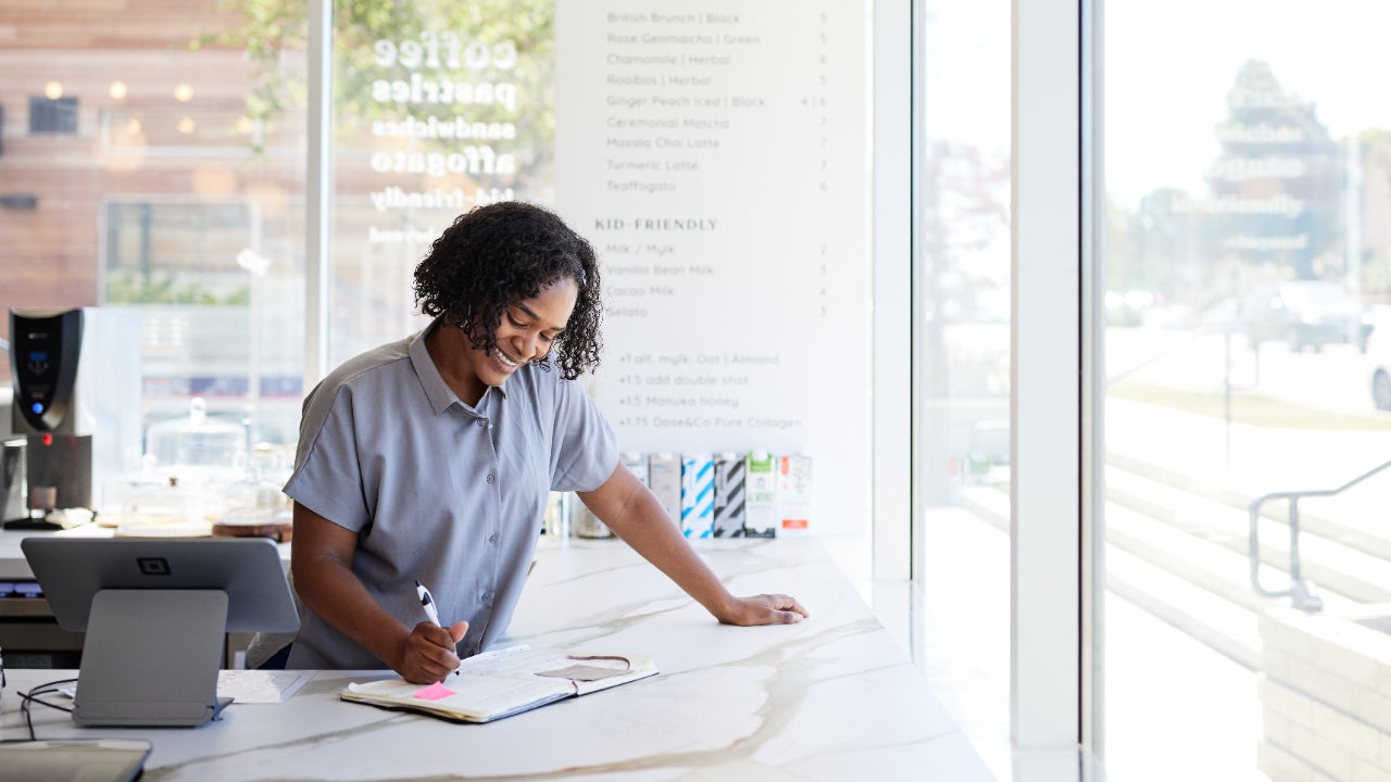 Female entrepreneur smiling while accounting on a checkout counter.