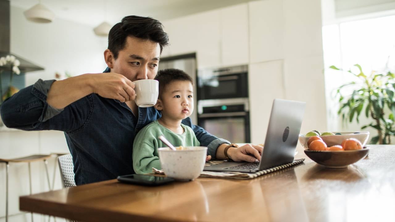 Father multi-tasking with young son (2 yrs) at kitchen table