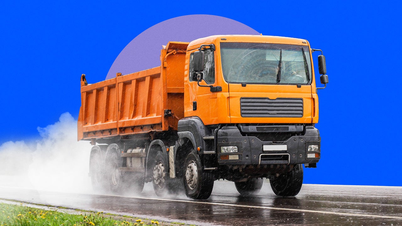 A dump truck is driven along a wet stretch of road.