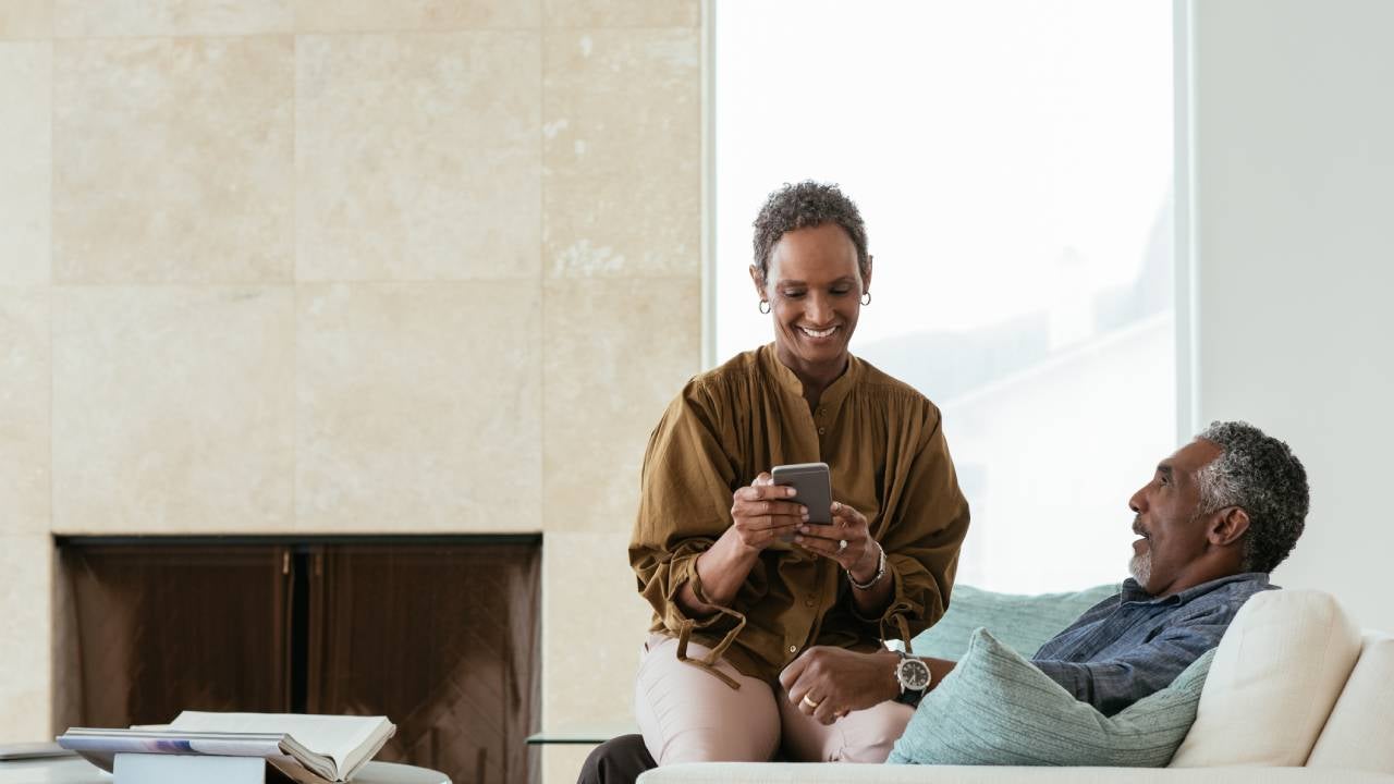 Smiling man looking at female partner with smart phone sitting on lap at home