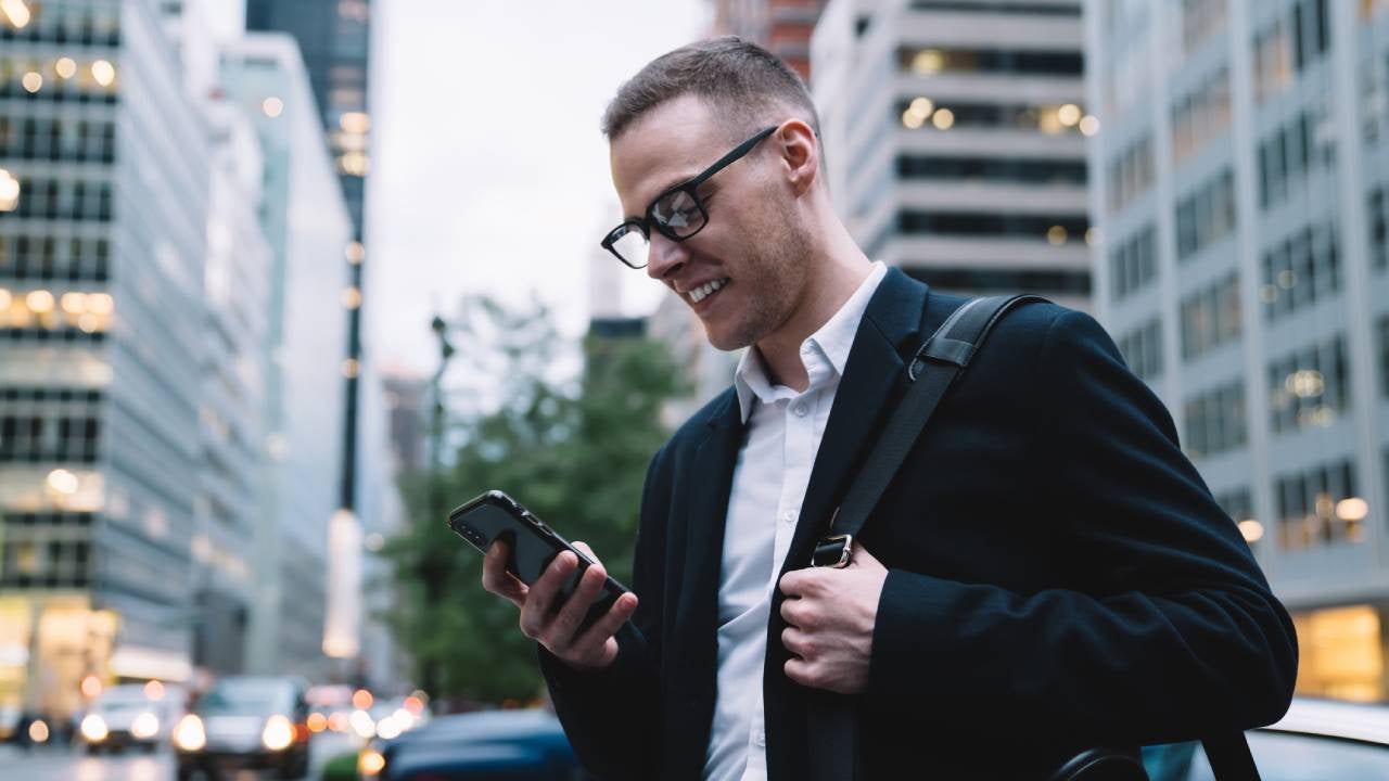 Man smiling at his cell phone in a busy downtown area