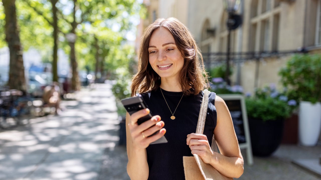 Smiling young woman with smartphone walking on the street