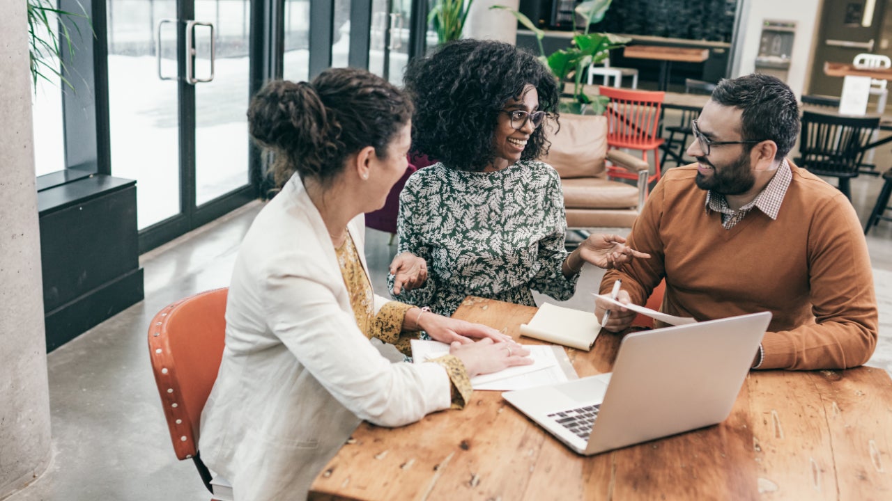 A man and two women review loan documents in an office with a laptop.