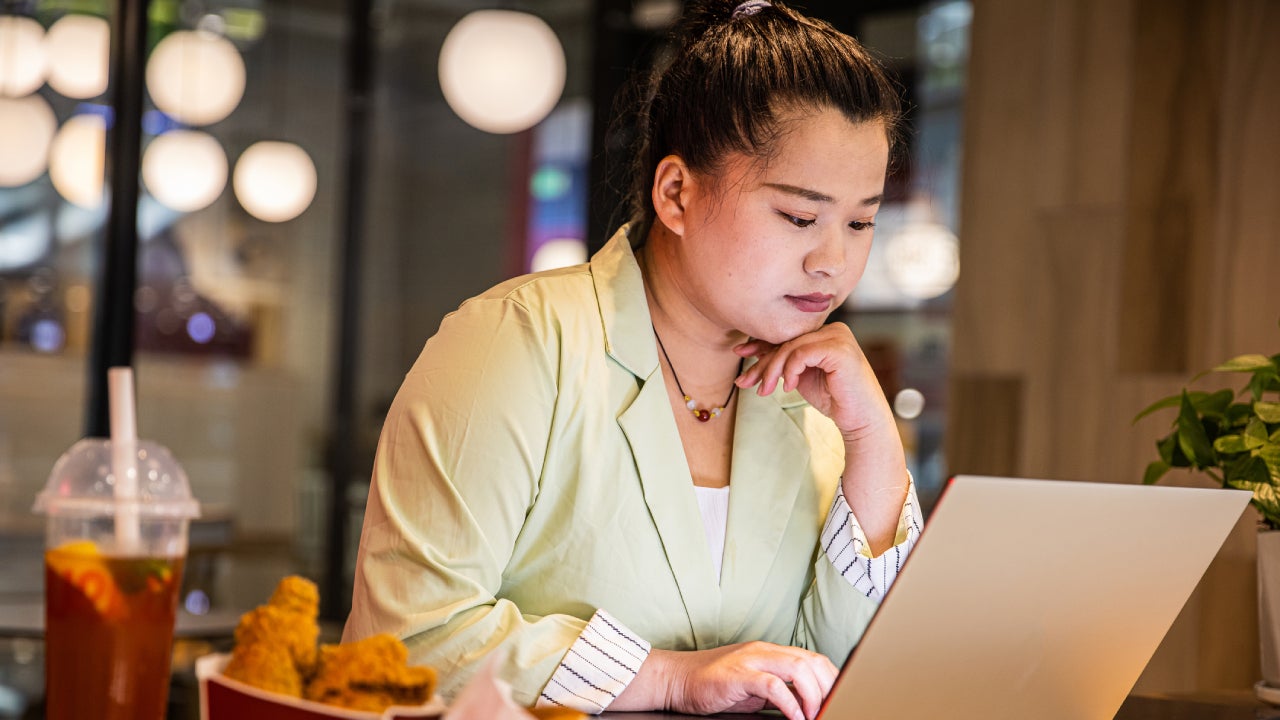 Businesswoman working at laptop with fast food on restaurant table