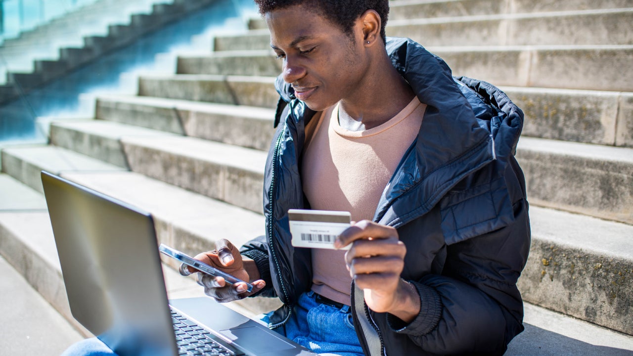 Gay guy sitting using laptop paying online with credit card, Lifestyle of gay guy on stairs using laptop, cell phone and credit card