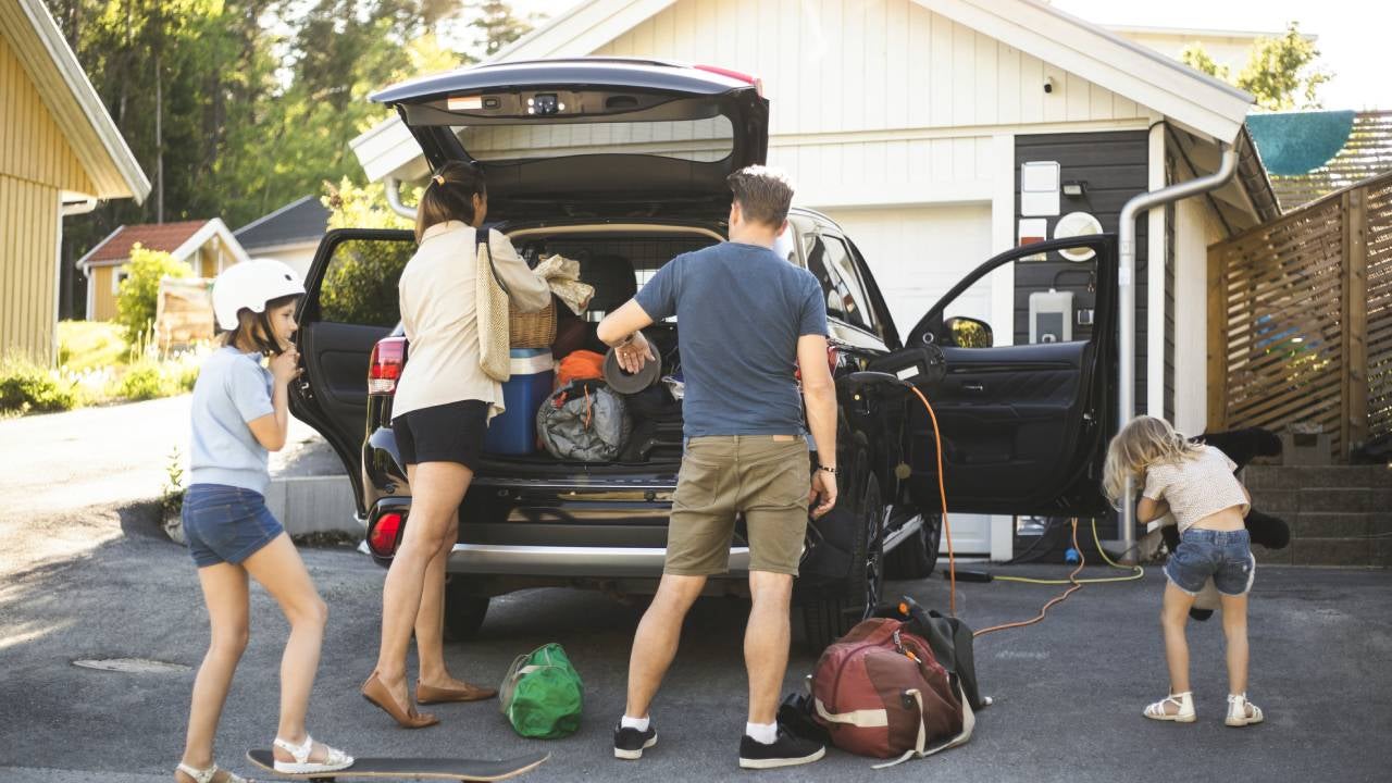 Portrait of mother, father and two daughters standing by car at electric vehicle charging station