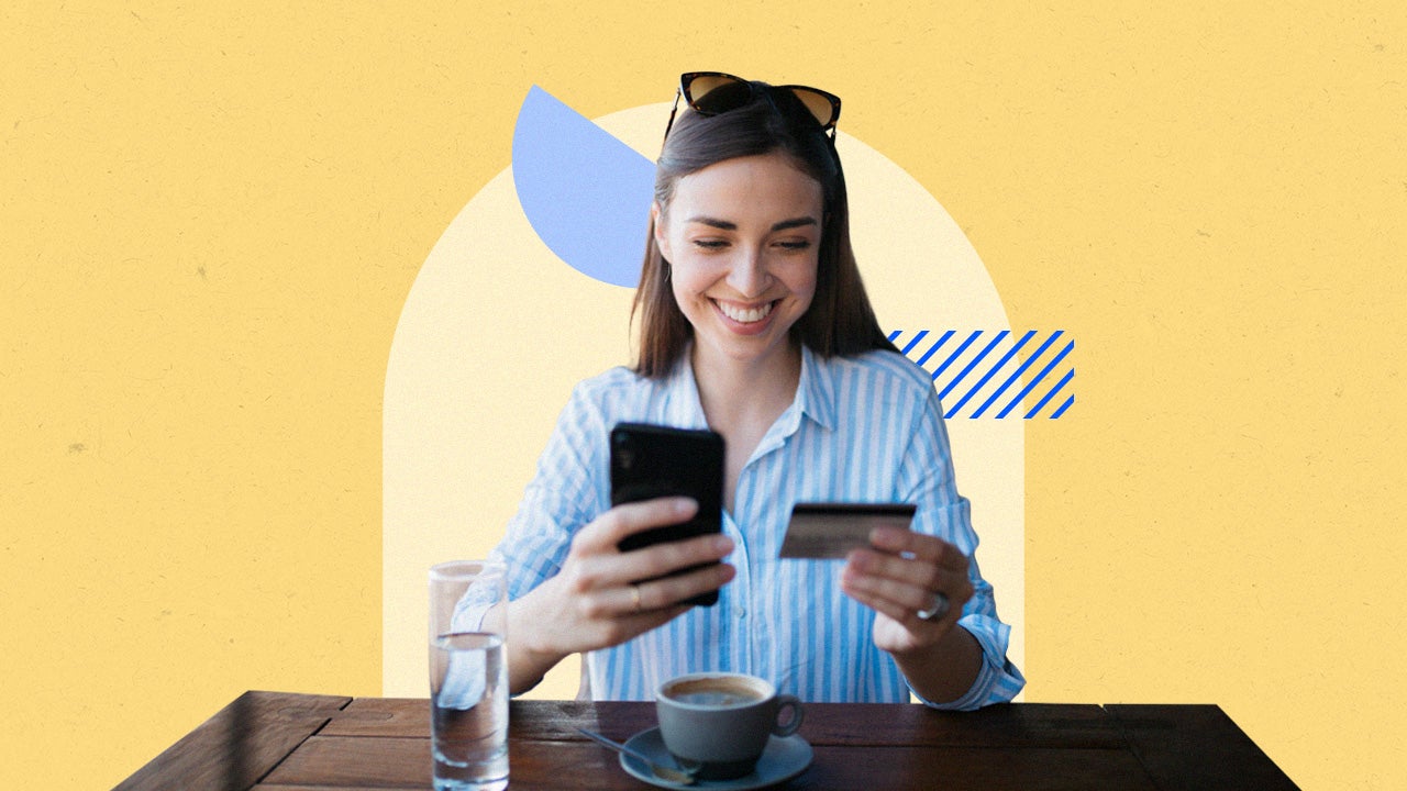 woman holding a credit card and phone in her hands while sitting down with coffee and a glass of water in front of her