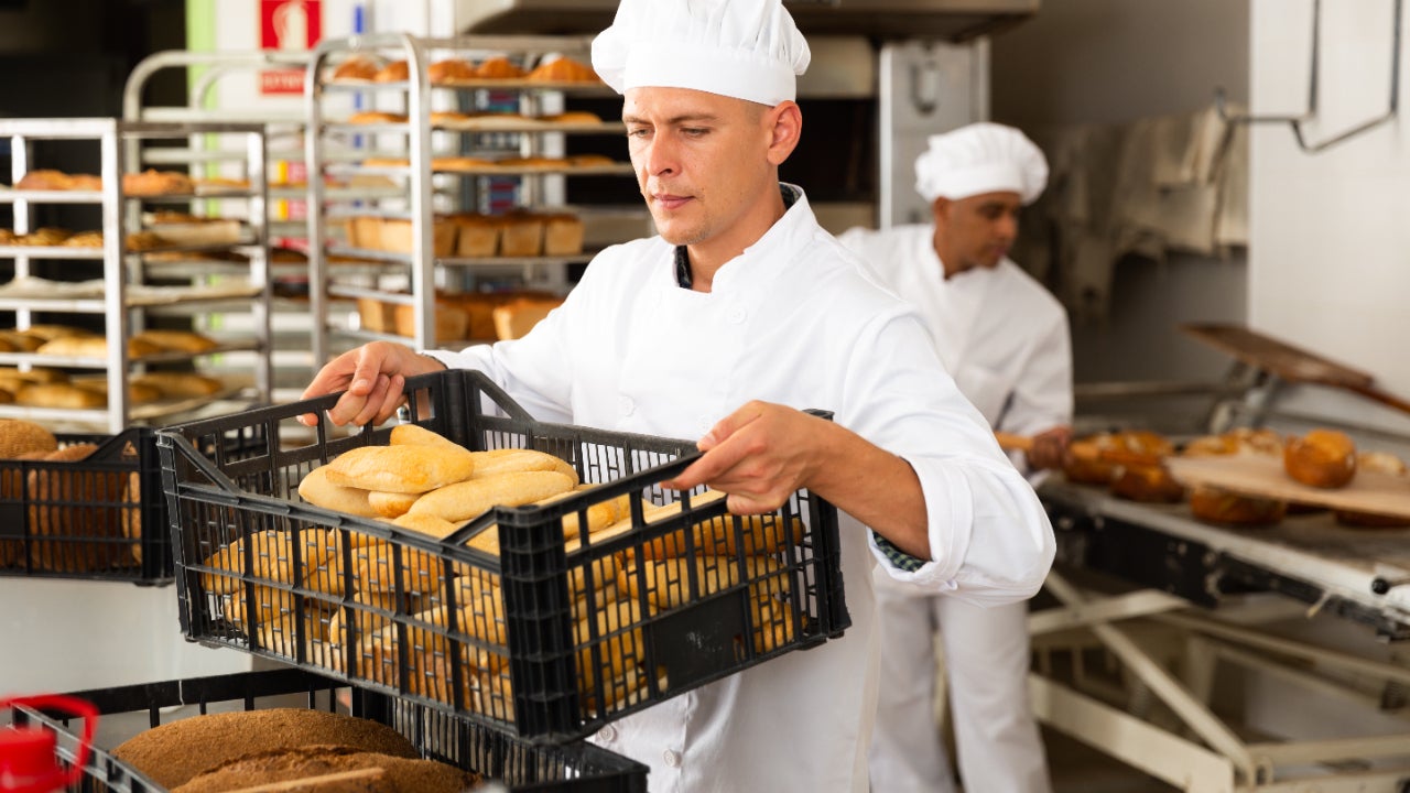 Male baker carrying a crate with baked bread in his bakery.