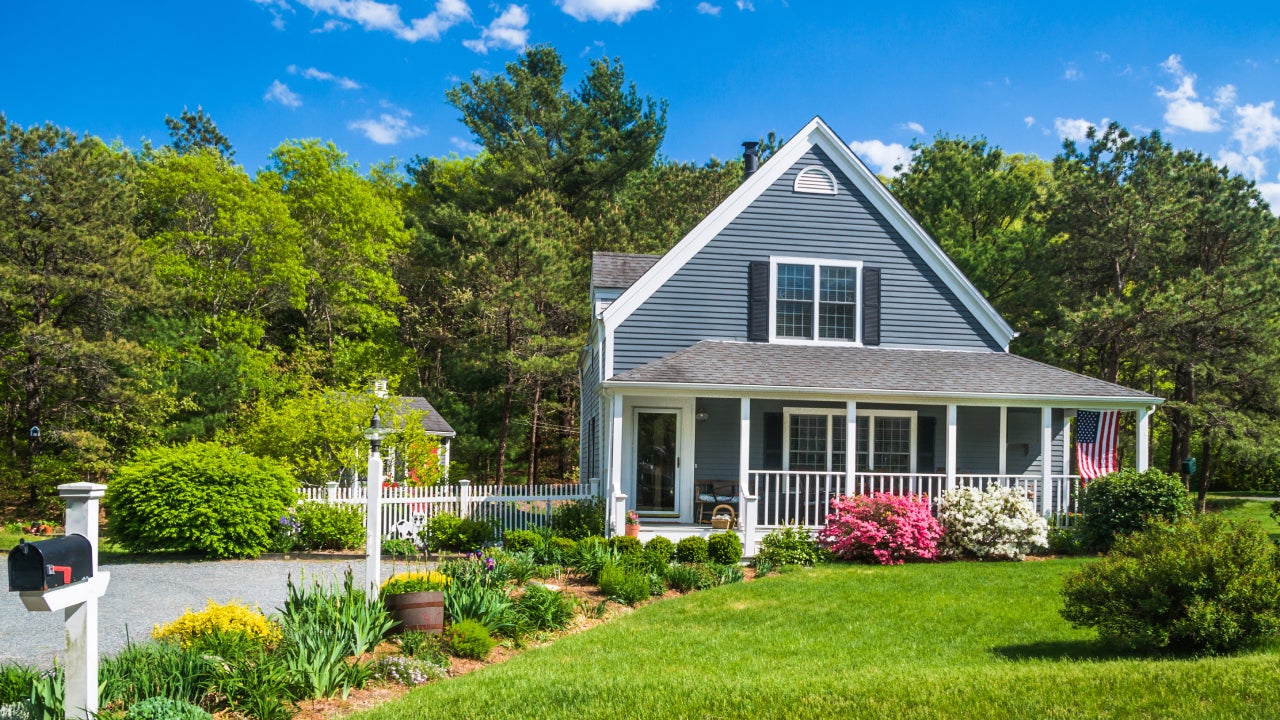 An American flag flies from the open porch and gardens surround a small single family home on a Spring afternoon on Cape Cod on the Massachusetts coast.