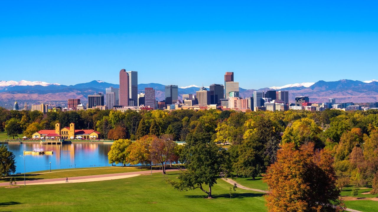 City skyline of Denver Colorado downtown with snowy Rocky Mountains and the City Park Lake.