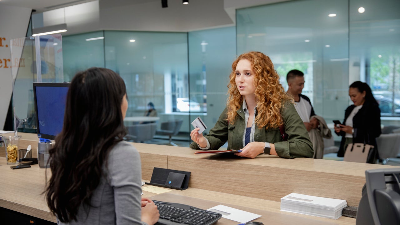 Young female client with debit card talking with bank teller in bank