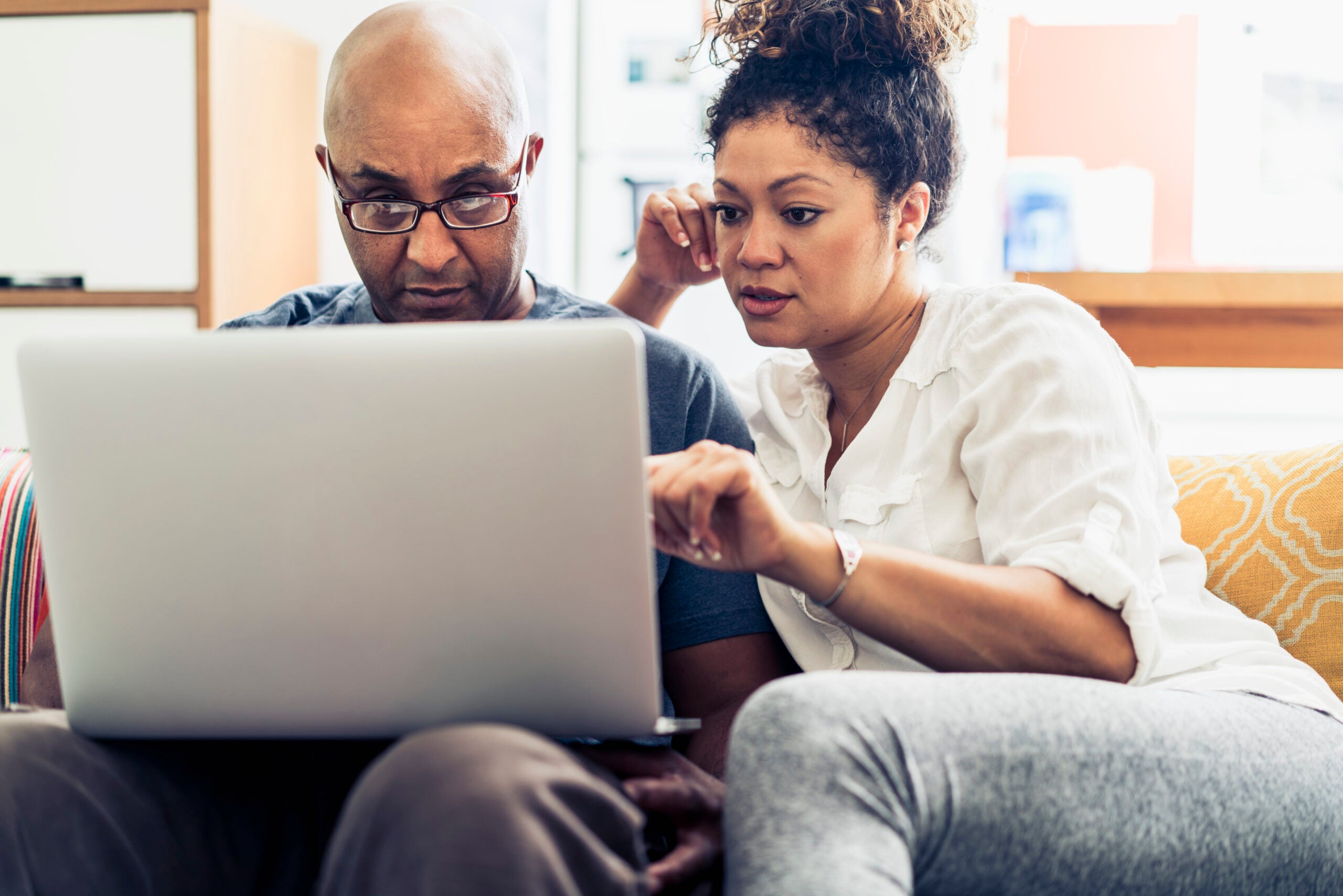 Couple looking at laptop while sitting on sofa at home