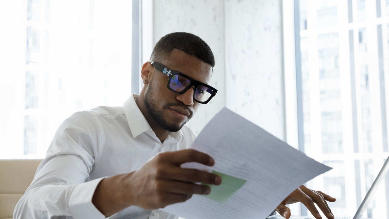 A small business owner sits in his office, looking over papers and working on his laptop.