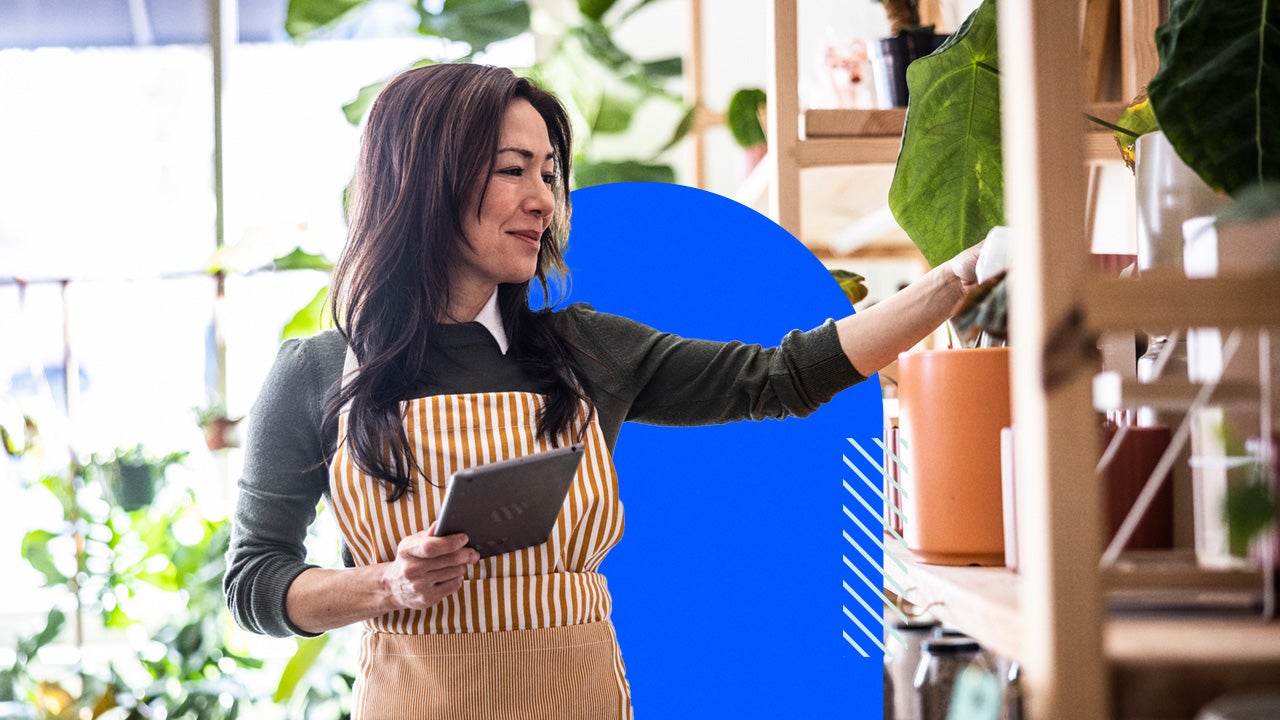 A shop owner in a striped apron holds a tablet.