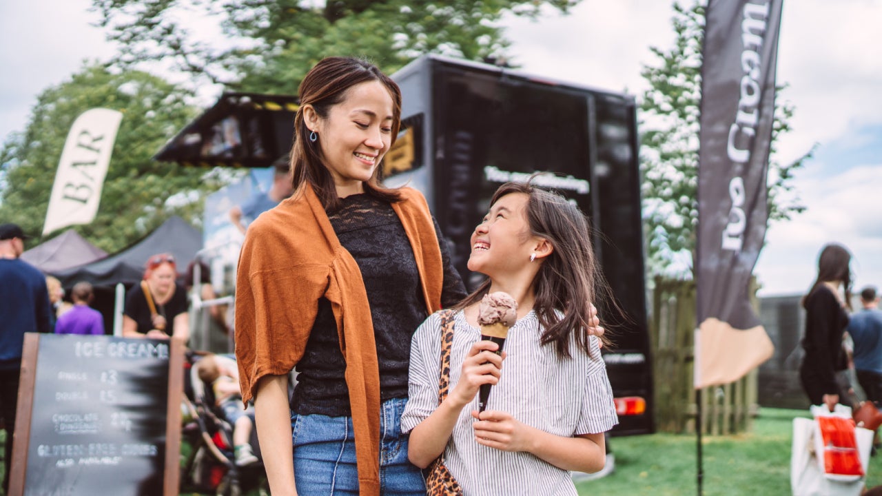 Lovely girl enjoying ice cream with her young pretty mom in front of a food truck at food festival