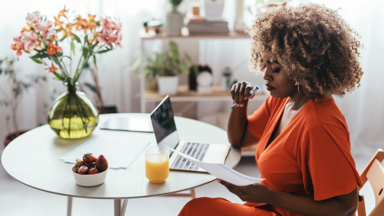 Black female entrepreneur working from home, sitting at the kitchen table and analyzing a report on her computer.