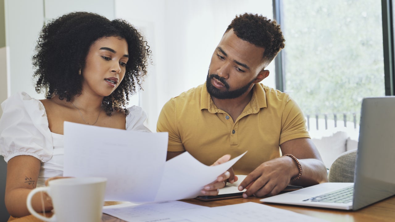 A couple reviews financial documents next to a laptop.