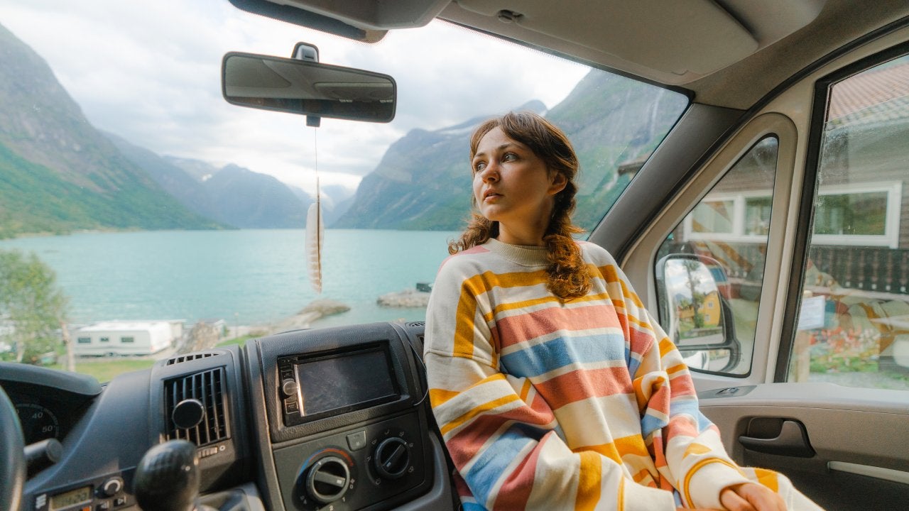 Silhouette of young woman sitting in camper van on passenger seat and looking through the window at sunset