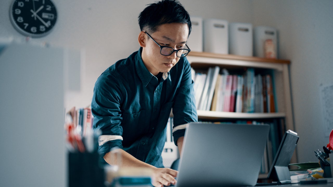 A man with glasses reviews notes on his computer at his office.