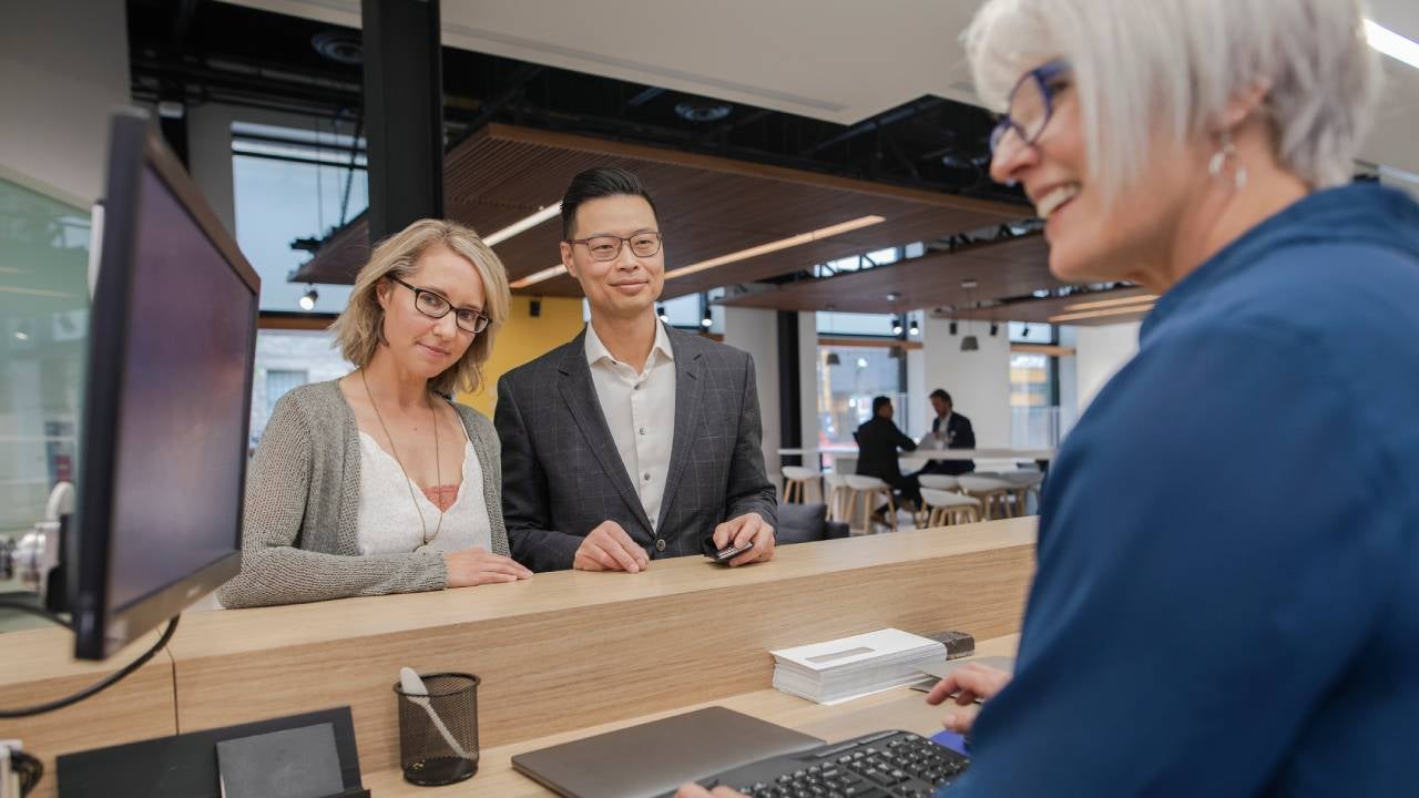 Bank teller at computer helping couple at bank branch counter