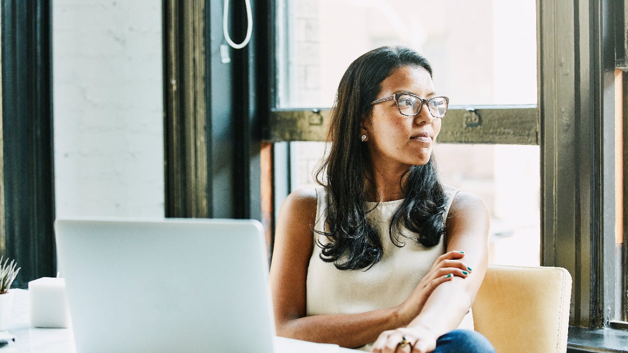 Person with glasses looking thoughtfully away from laptop