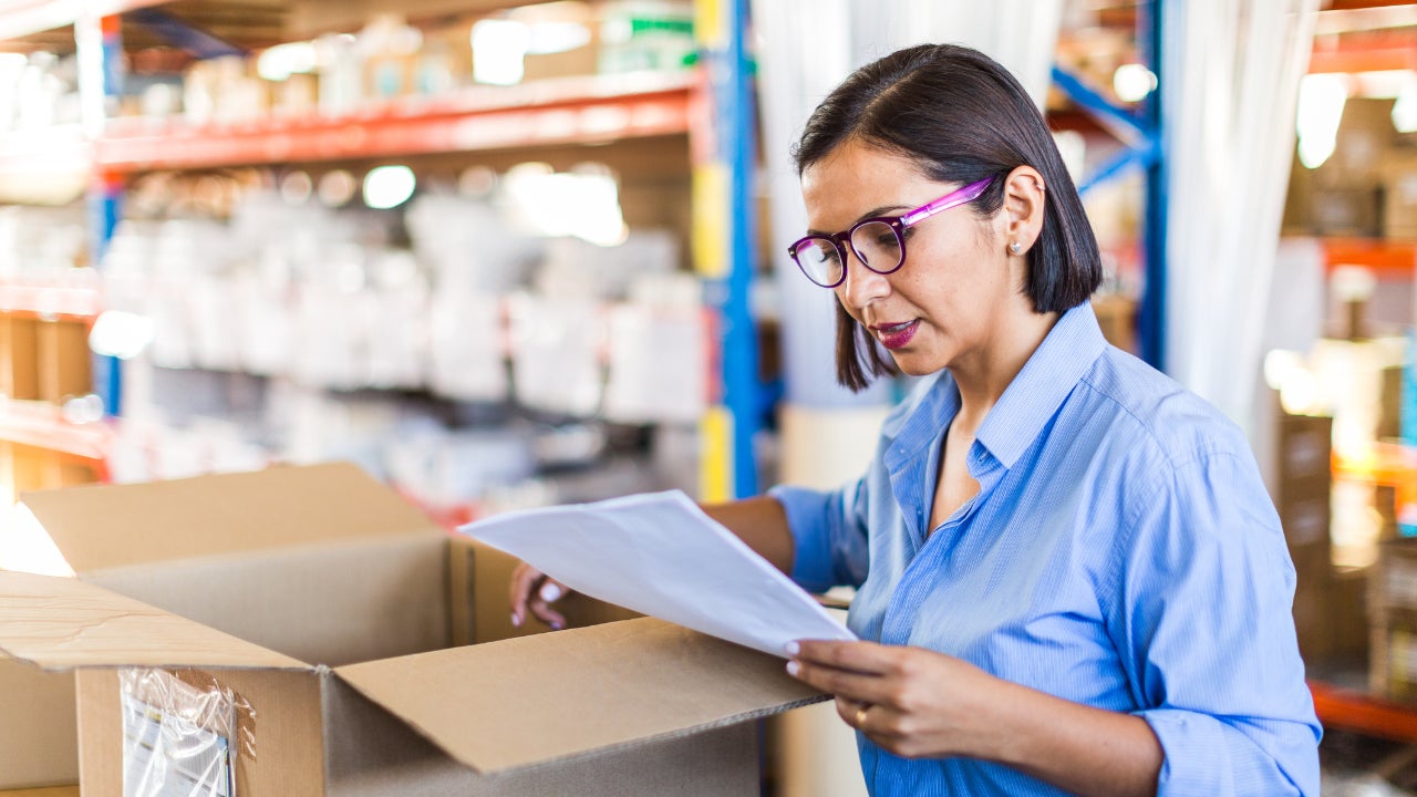 A female business owner looks over an invoice and supplies inside a box.