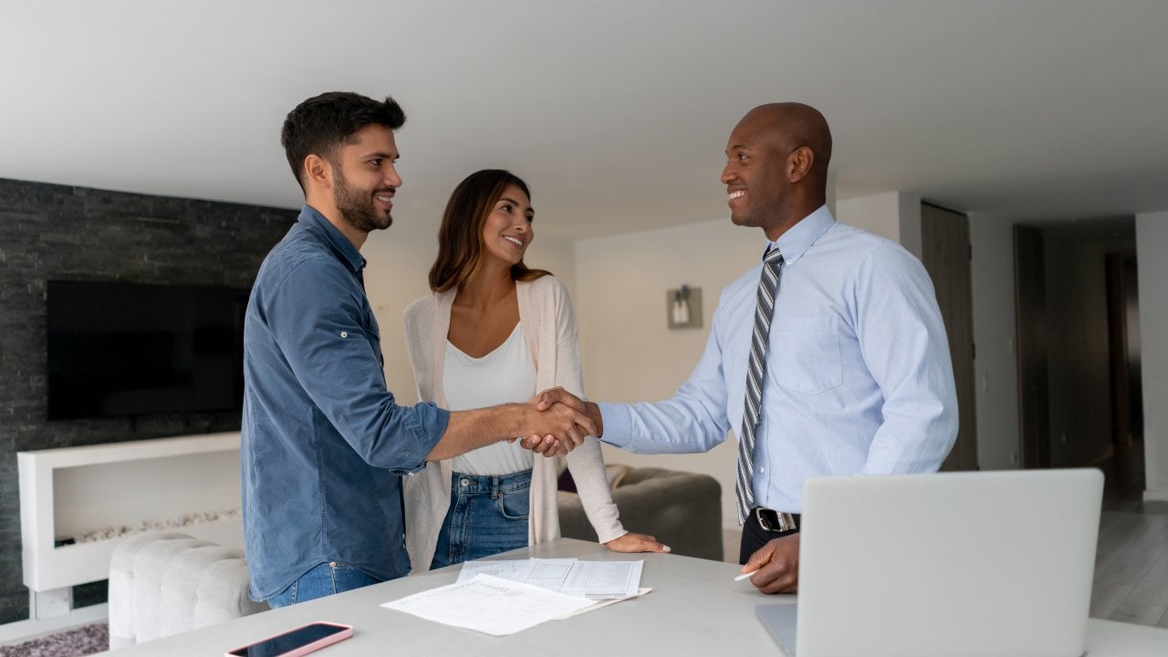 Couple buying a house and closing the deal with the Real Estate Agent with handshake