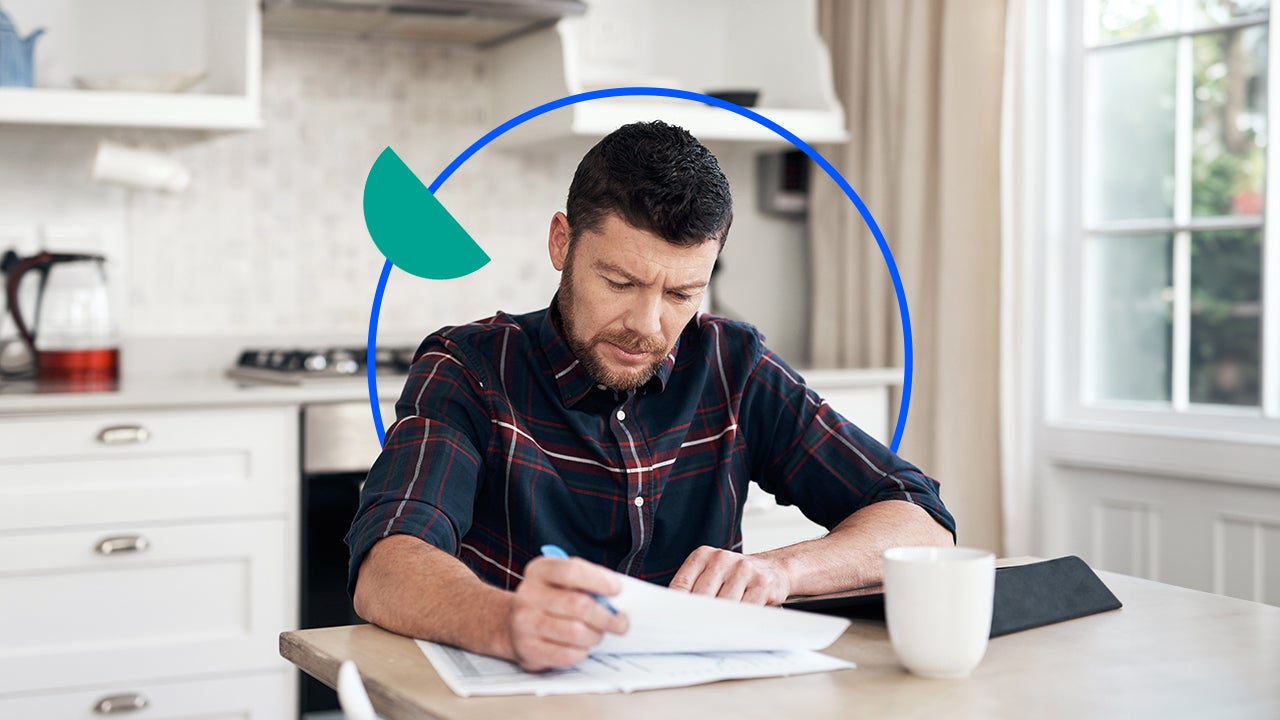 Middle aged white man sits at a kitchen table while reviewing paperwork.