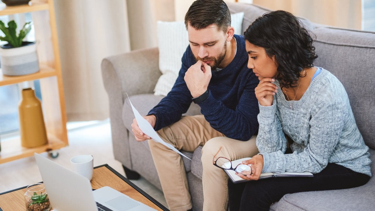 Young couple sitting on the sofa at home together and calculating their finances