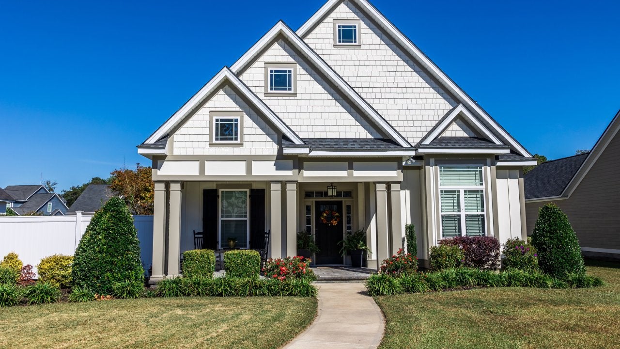 The front view of a cottage craftsman style white house with a triple pitched roof with a sidewalk, landscaping and curb appeal