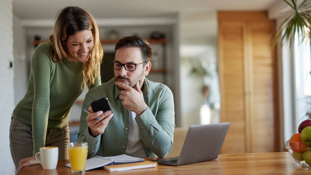 Young couple reading a text message on smart phone while working at home.