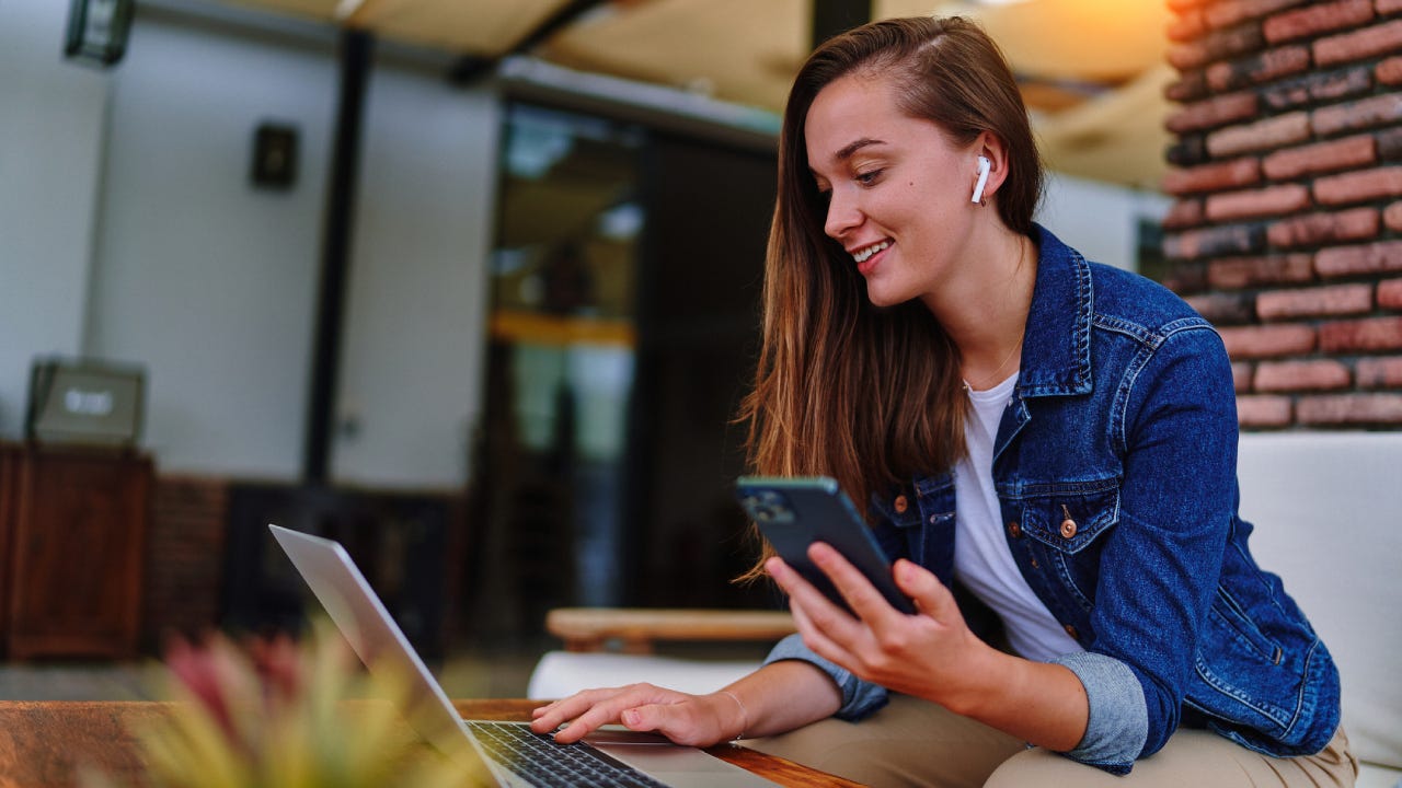 Young woman wearing white headphones using laptop and mobile phone for remote work