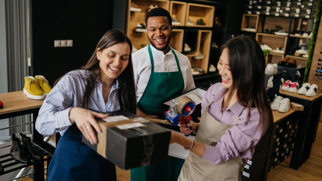 A businesswoman helps her employees package shoes for shipping.