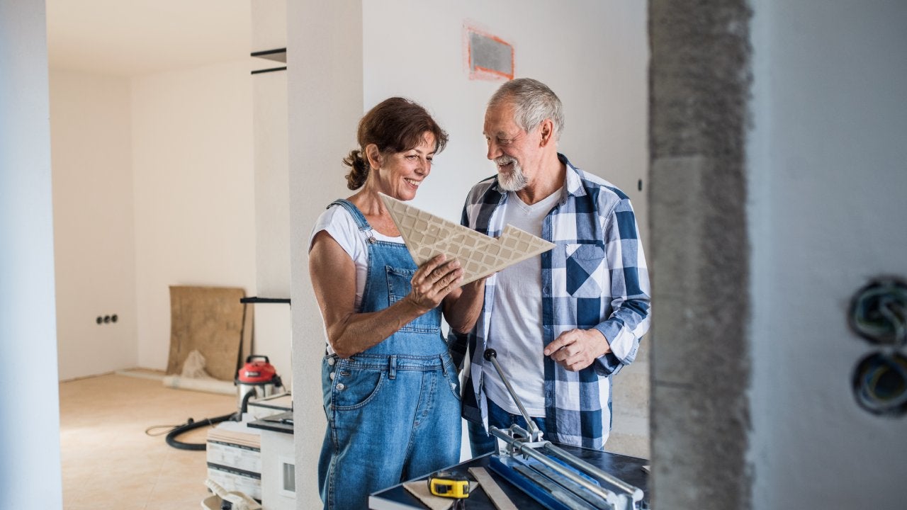 Senior couple laying tile floor in new home