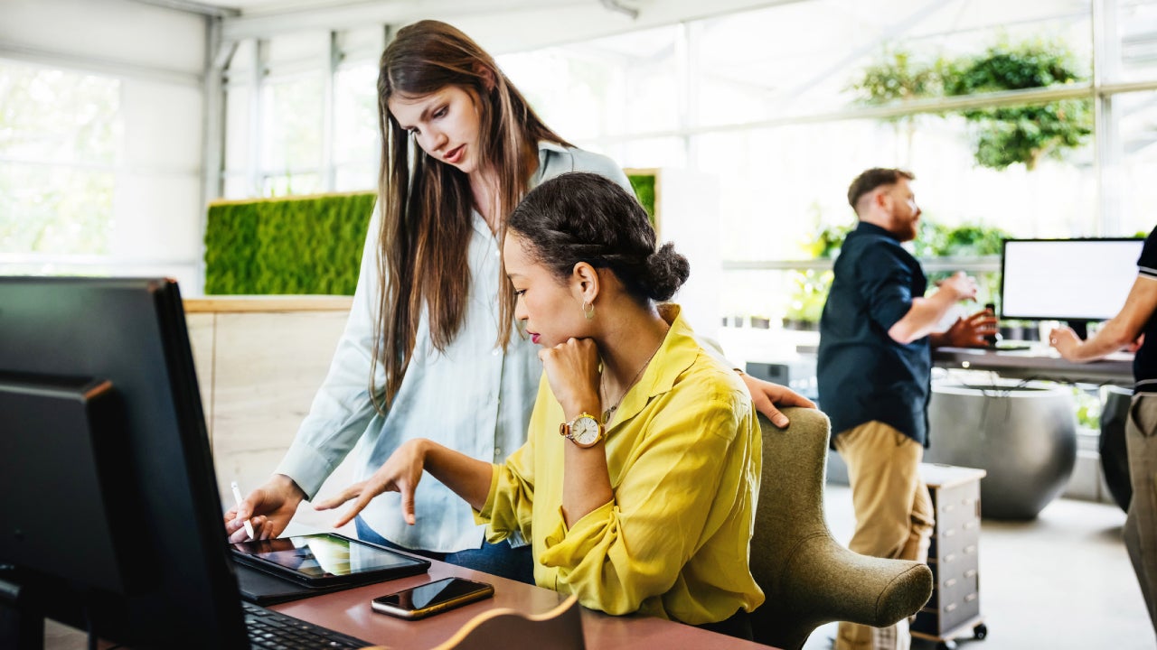 Two coworkers talking around a desk and computer