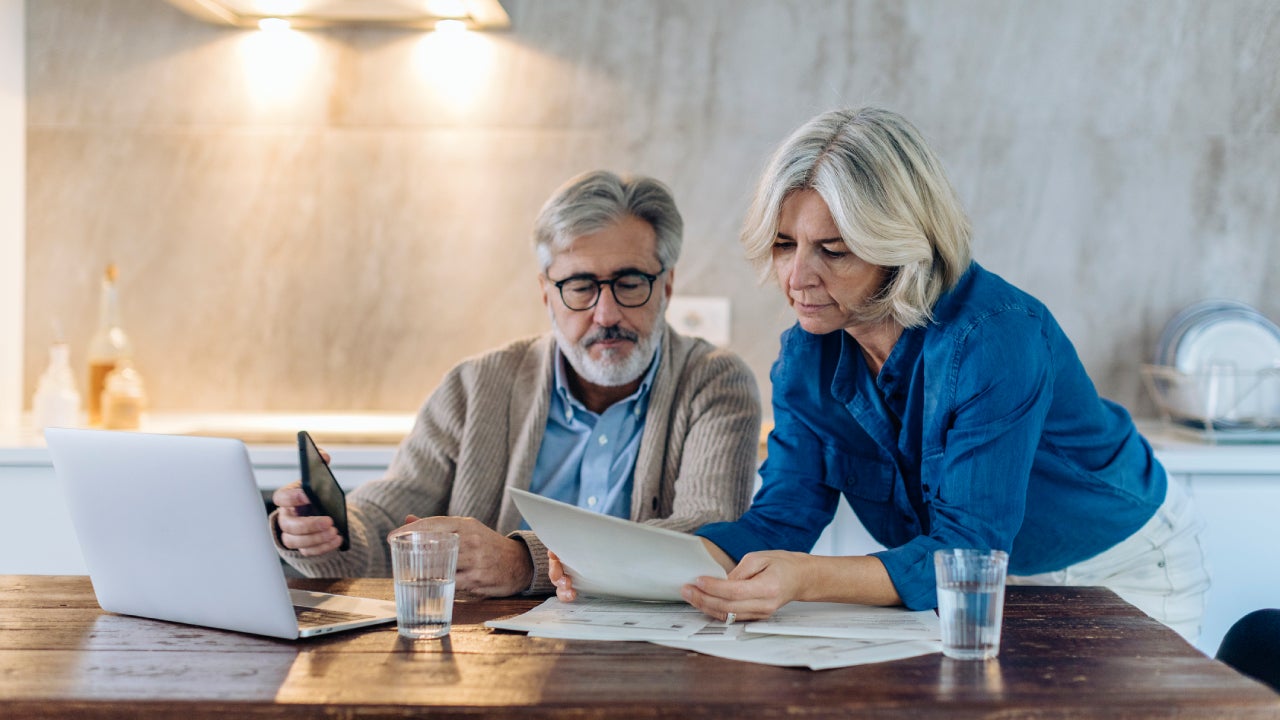 Old couple with papers and laptop on kitchen table at home