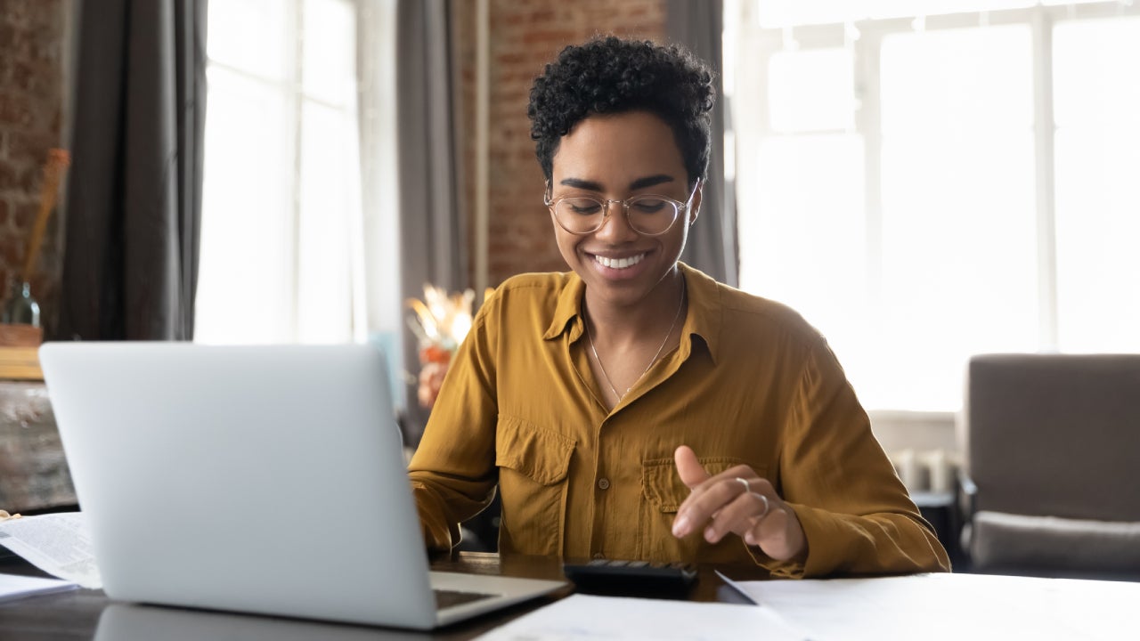 woman in glasses counting profit, on calculator at laptop computer