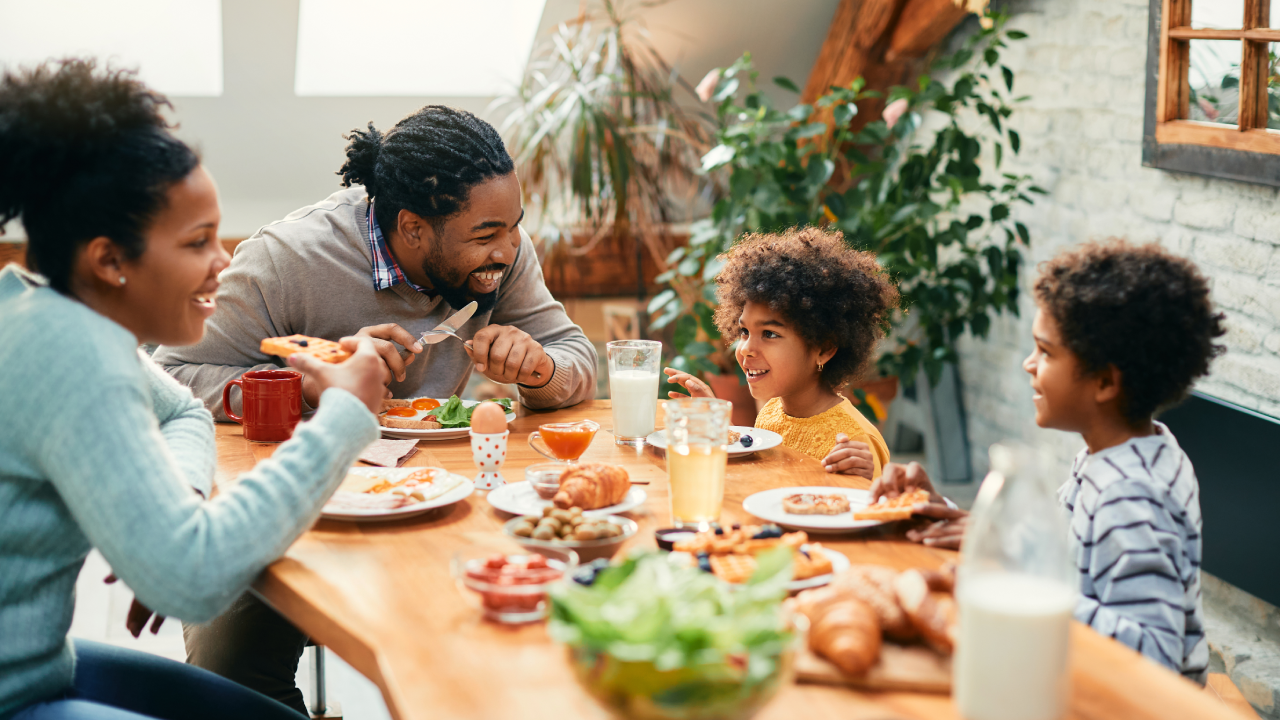 Happy black parents and their kids talking while having breakfast together in dining room.