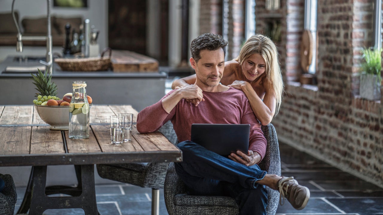 couple siting in country house kitchen, looking at laptop