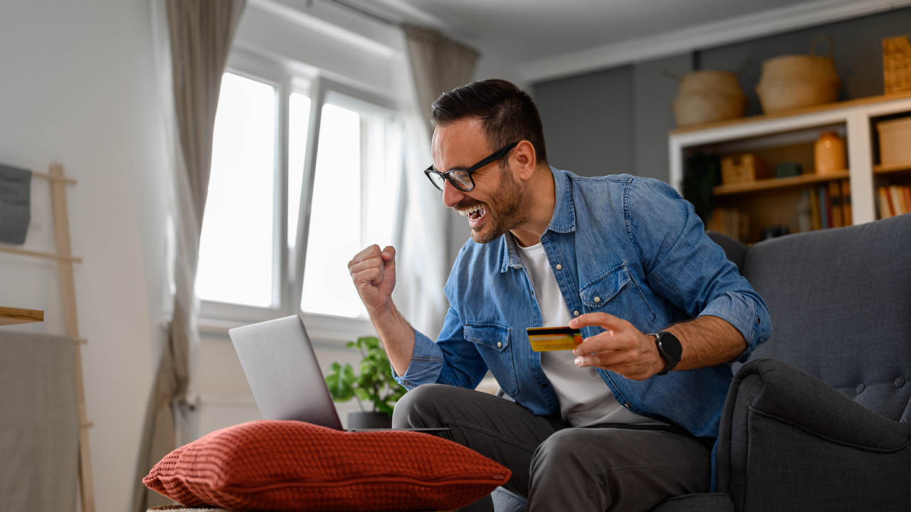 Businessman with credit card pumping fist and screaming in joy while doing online shopping on laptop