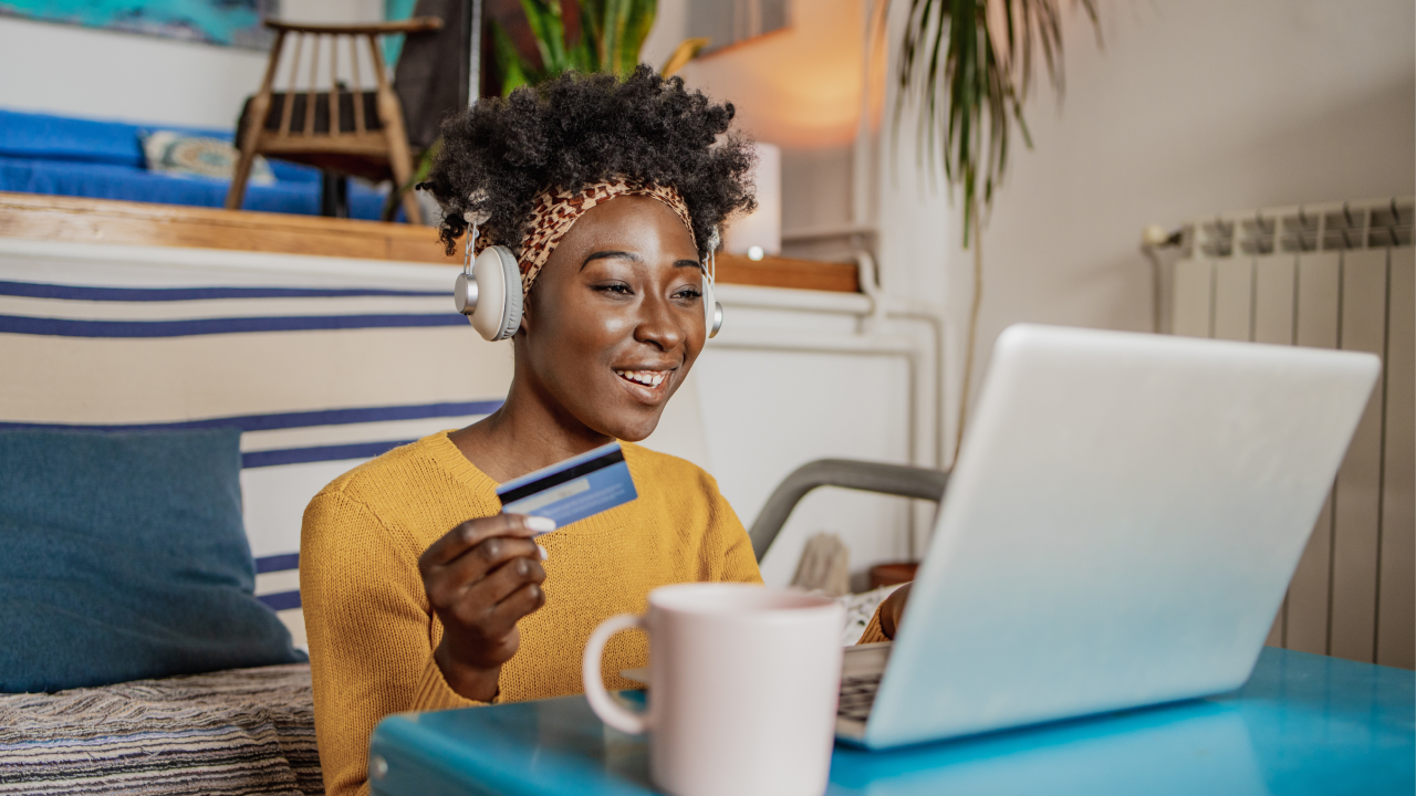 A young woman is in the living room, she is using a laptop and credit card