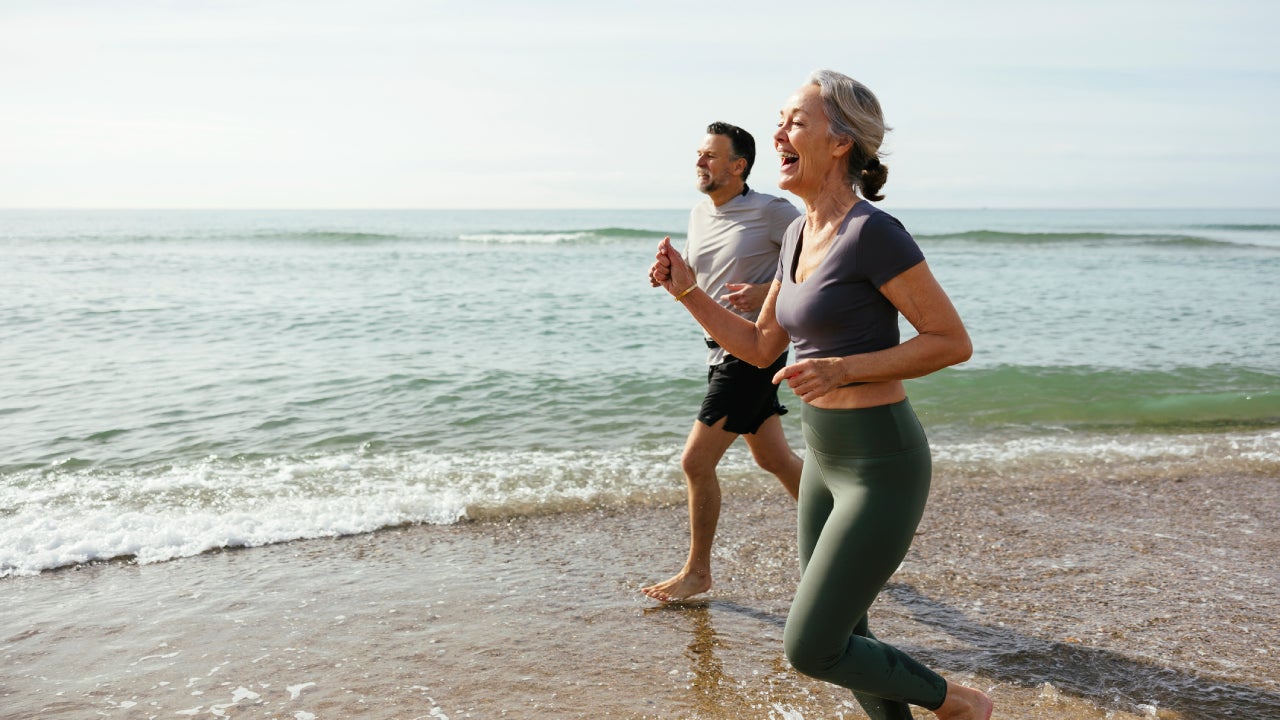 Happy mature couple laughing and running in water at beach