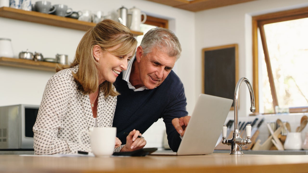 A senior couple planning their finance and paying bills while using a laptop at home.