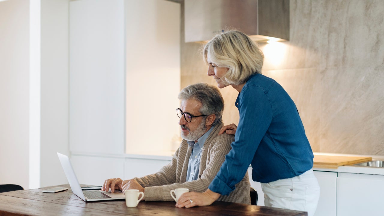 man with wife using laptop on kitchen table at home