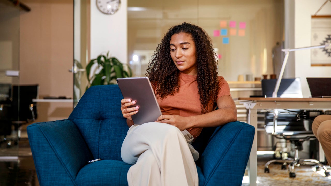 Woman sitting on a blue armchair reviewing a tablet